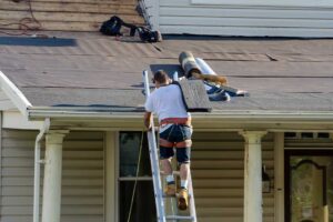 A person examining worn shingles and tiles on a sun-exposed residential rooftop.