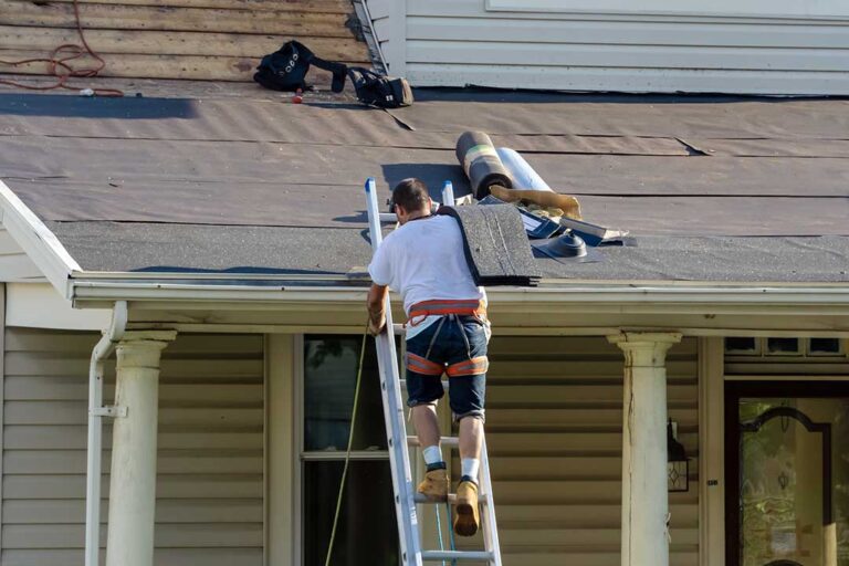 A person examining worn shingles and tiles on a sun-exposed residential rooftop.
